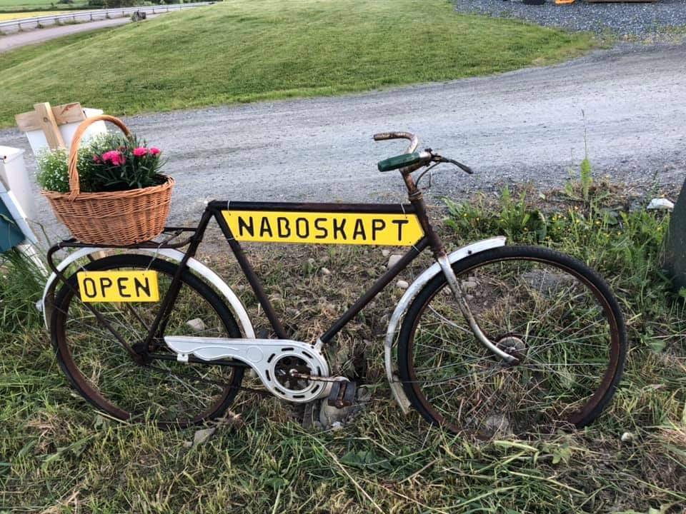 Gammel sykkel med blomsterkurv og skilt med teksten NaboSkapt og Open
